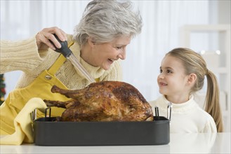 Grandmother and daughter basting roast turkey.