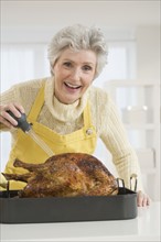 Senior woman basting roast turkey.