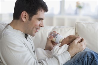 Father feeding newborn baby on sofa.