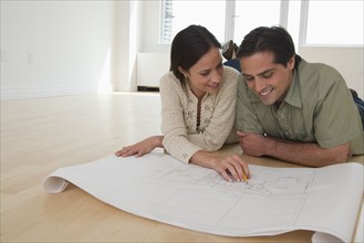 Couple laying on floor looking at blueprints.