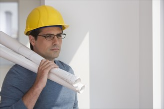 Man wearing hard hat and holding blueprints.
