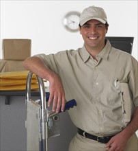 Deliveryman smiling and leaning on hand truck.