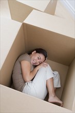 Woman curled up in empty moving box.