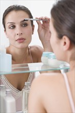 Woman combing eyebrows in mirror.