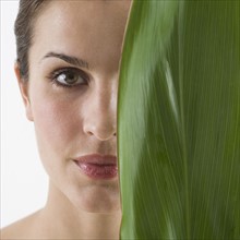 Woman holding leaf over half of face.