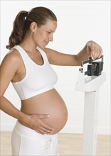 Pregnant woman weighing self on scale.