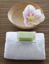 Soap and towel next to bowl of water with flower.