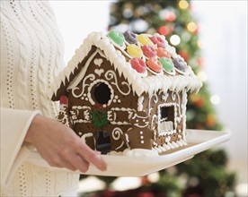 Woman holding gingerbread house on tray.