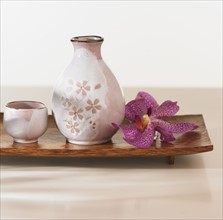 Close up of jug and cup with flower on tray.