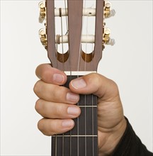 Close up of man's hand holding neck of guitar.