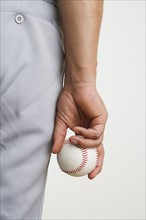 Close up of man holding baseball at side.