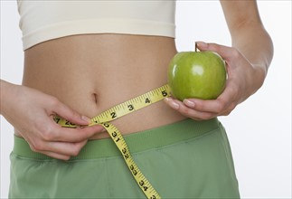 Studio shot of woman holding apple and measuring her waist.