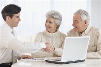 Businessman shaking hands with senior couple in home.