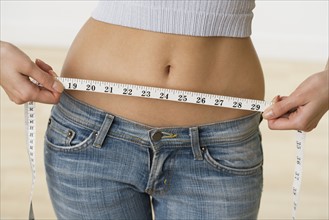 Woman with bare midriff measuring waist.
