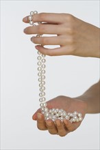 Close up studio shot of woman's hands holding pearl necklace.