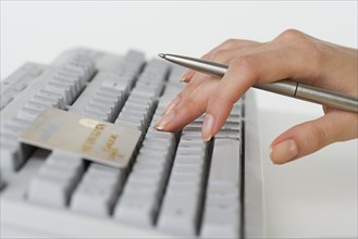 Close up of woman's hand holding pen with credit card and computer keyboard.