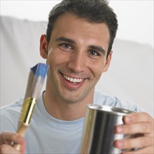 Man smiling and holding paintbrush and paint can.