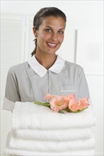 Female maid holding stack of towels with flowers.