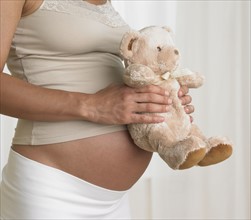 Pregnant woman holding teddy bear against stomach.