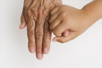Close up of child's hand holding pinky finger on senior's hand.