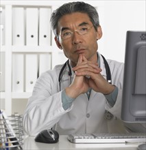 Senior male doctor sitting at computer.
