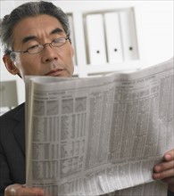 Senior Asian businessman reading newspaper.