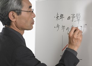 Senior Asian businessman writing on white board.