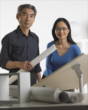 Asian businessman and businesswoman at drafting table with blueprints.