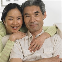 Middle-aged Asian couple hugging and smiling.