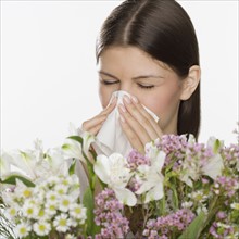 Woman blowing nose next to flowers.