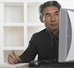 Senior Asian businessman looking at computer and writing.
