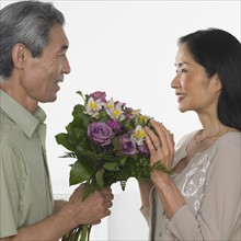 Asian man giving Asian woman bouquet of flowers.