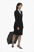 Studio shot of businesswoman pulling suitcase.