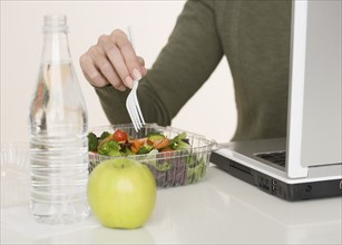 Woman eating salad next to laptop.