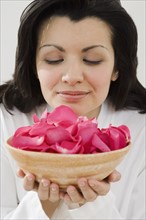 Woman smelling bowl of flower petals.