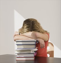 Woman resting head on stack of books.