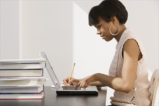 African woman typing on laptop next to stack of books.