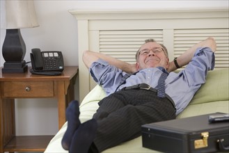 Businessman laying on bed in hotel room.