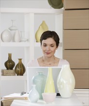 Woman looking at laptop in pottery store.