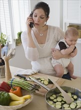 Mother holding baby, talking on telephone and cooking.