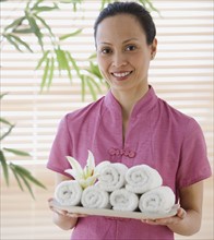 Asian woman holding tray of rolled towels.