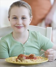 Girl eating spaghetti and meatballs.