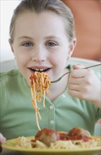 Girl eating spaghetti and meatballs.