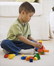 Asian boy playing with blocks on floor.