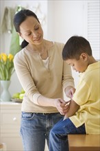Asian mother putting bandage on son.