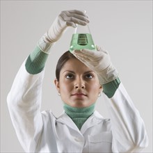 Indian female scientist looking at beaker of liquid.