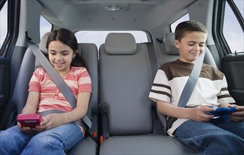 Brother and sister playing video games in car.