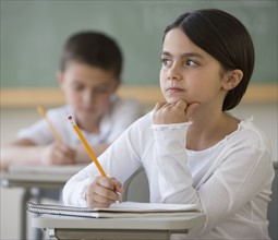 Girl thinking at desk in classroom.