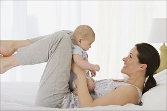 Mother playing with baby on bed.