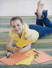 Girl cutting construction paper on floor.